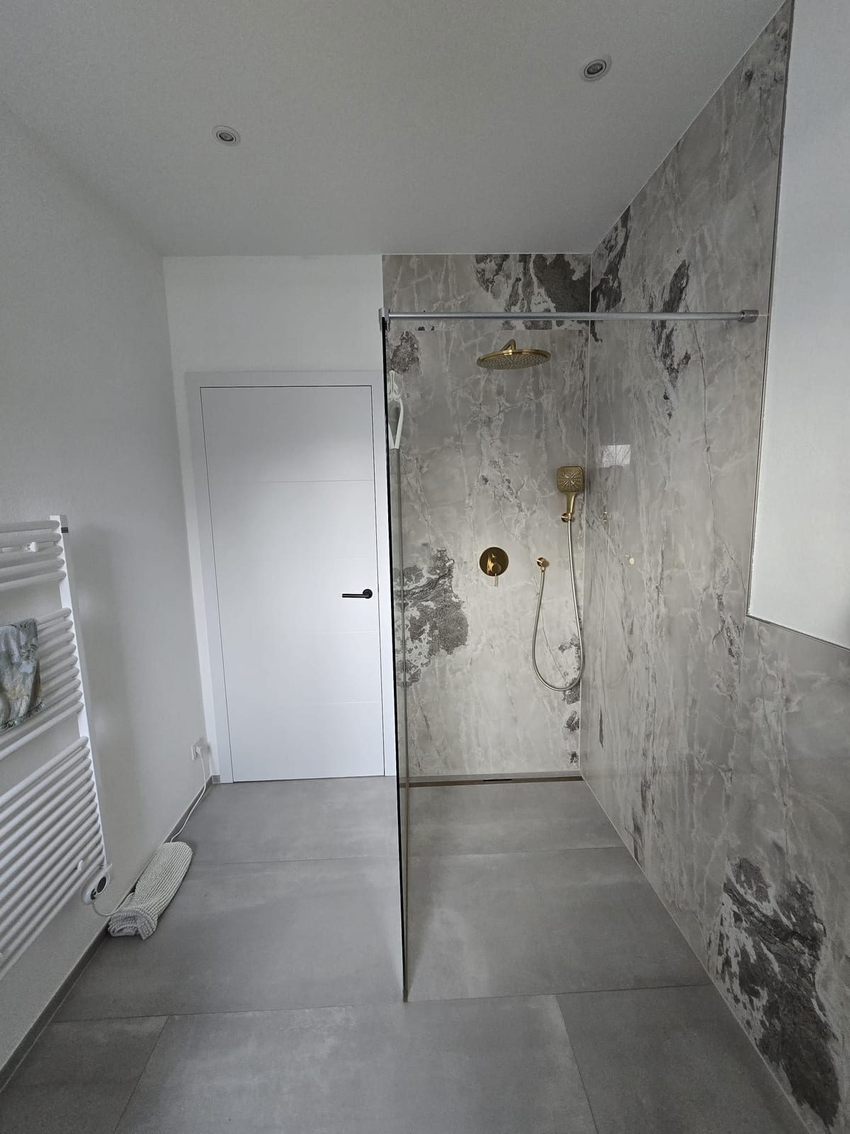 Ebenerdige Dusche mit ausdrucksstarker grau-weißer Marmorwand und goldfarbenen Armaturen