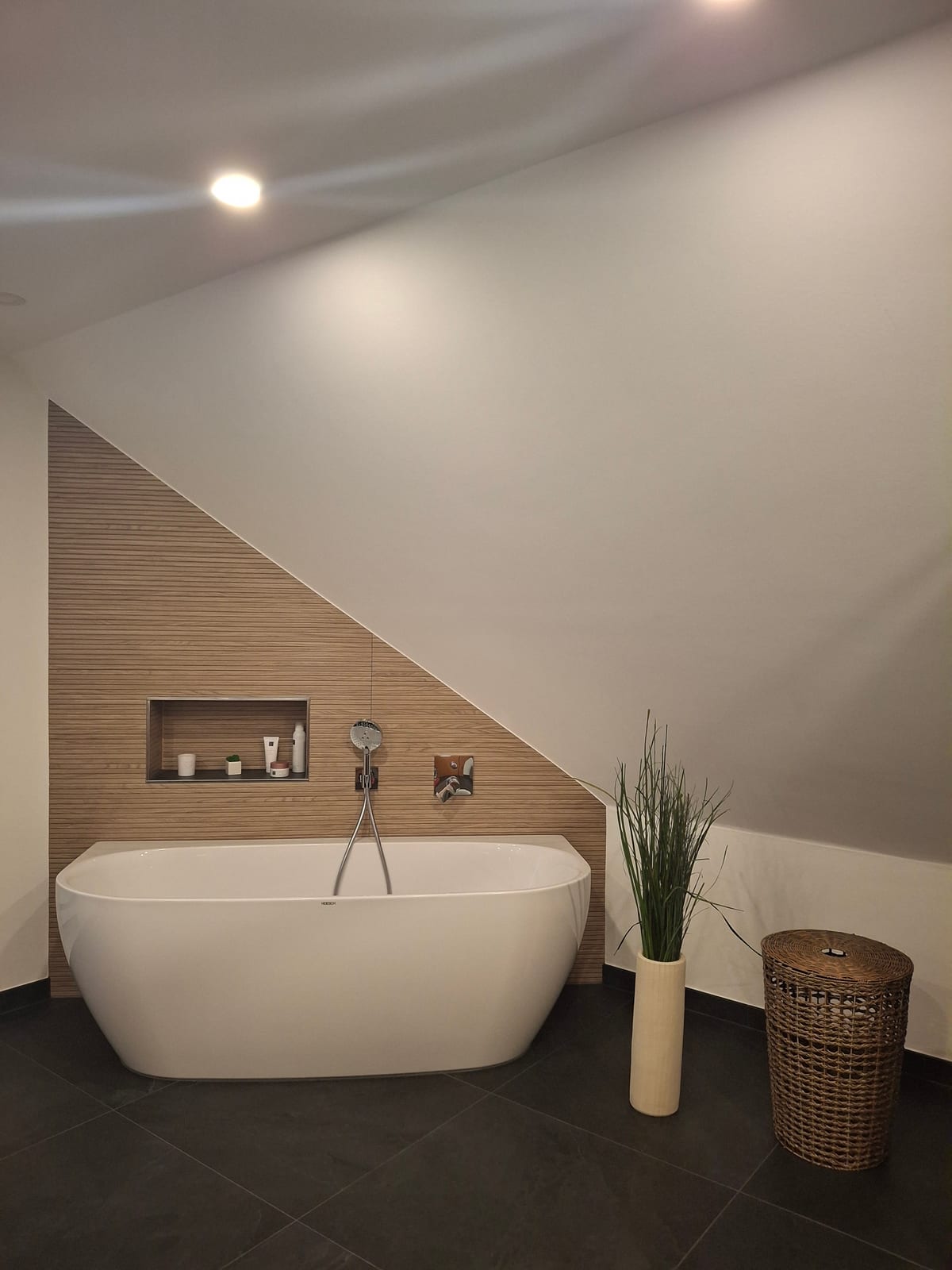Freistehende Badewanne vor einer Akzentwand in Holzoptik unter einer Dachschräge