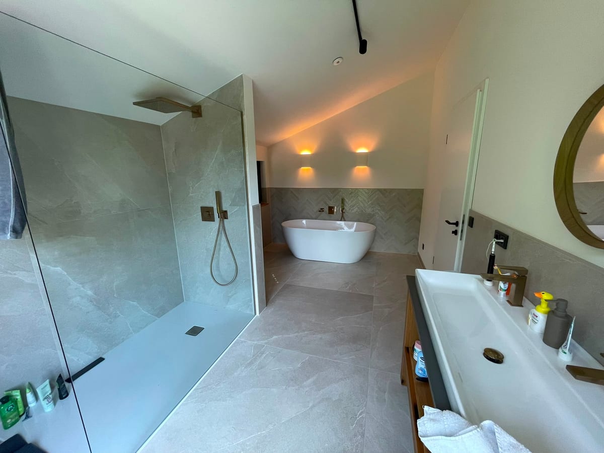 Luxuriöses Badezimmer mit ebenerdiger Marmordusche, freistehender Wanne vor Fischgrätenwand und Doppelwaschtisch