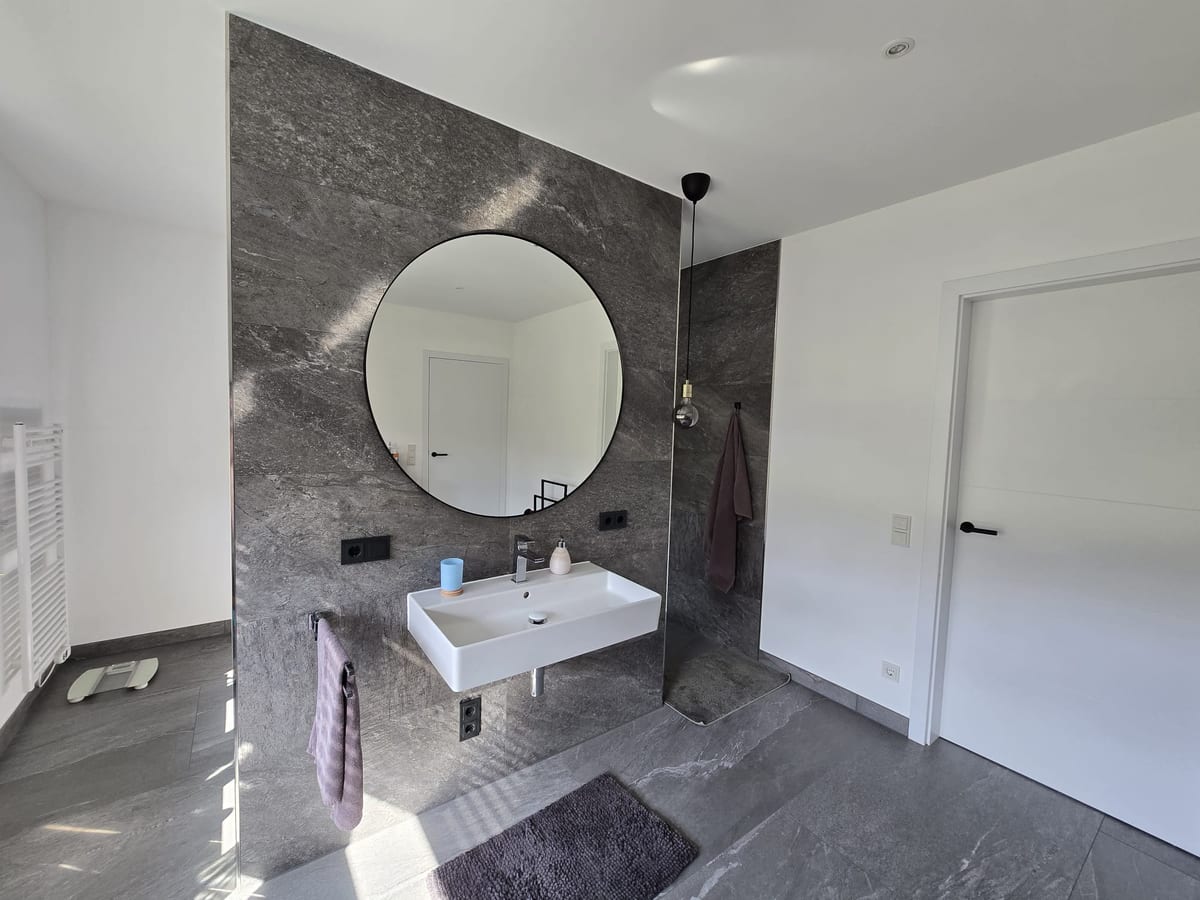 Badezimmer mit Aufsatzbecken, rundem Spiegel und grauer Wand in Marmoroptik