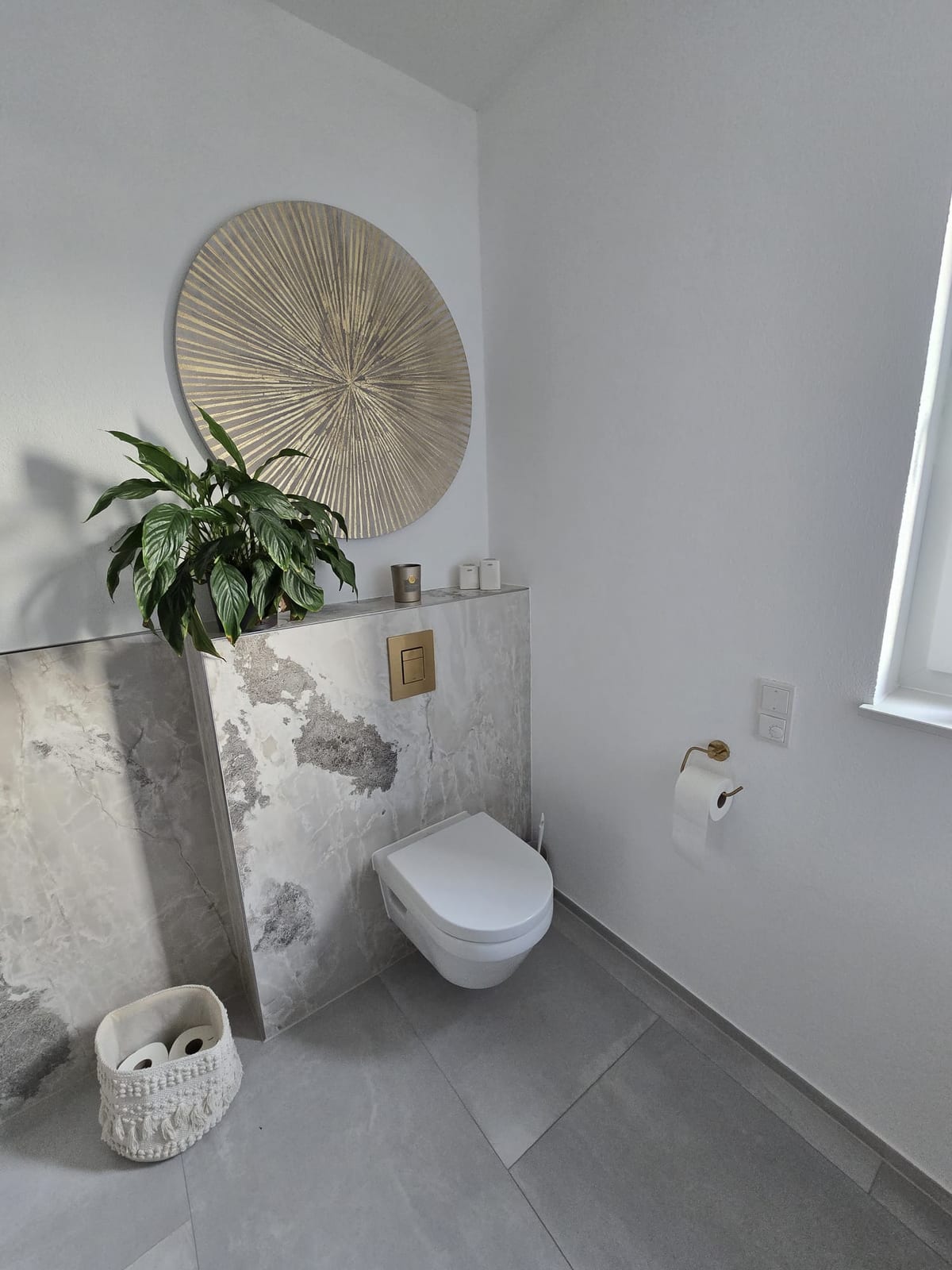 Akzentwand in Marmoroptik mit Wand-WC und rundem Rattanspiegel