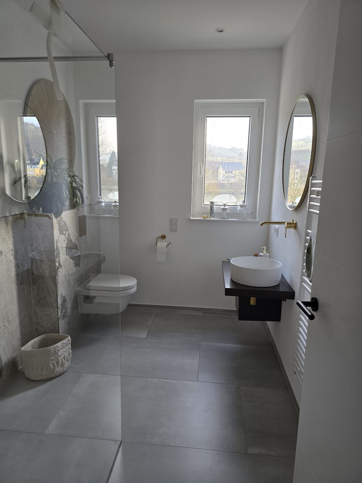 Helles Badezimmer mit zwei Rundspiegeln, bodengleicher Dusche und Blick über die Weinberge